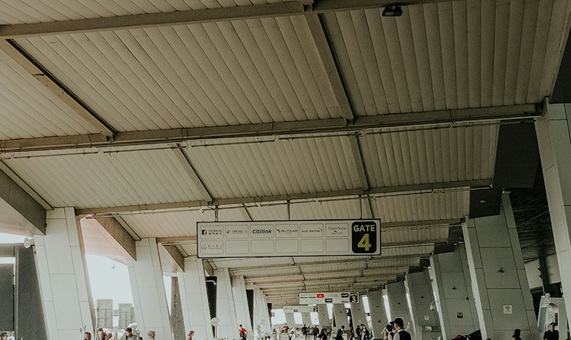 A busy airport terminal interior showing Gate 4 and Gate 3 signage with various airline logos, under a high industrial ceiling.